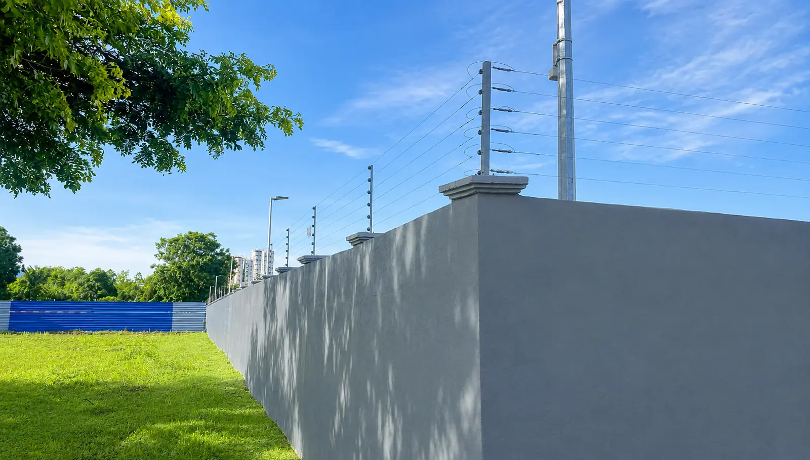 Electric fence following a long boundary wall beside an open landscaped site.