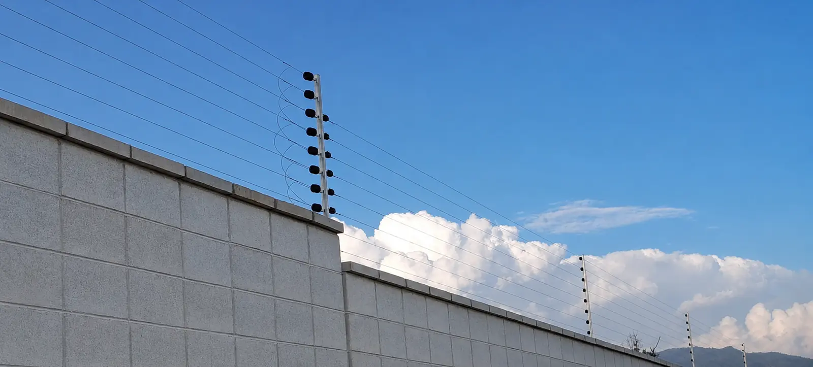 Eight-wire electric fence mounted along a concrete compound wall