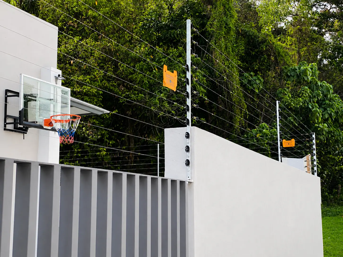 Electric fence system protecting a gated home beside tropical greenery