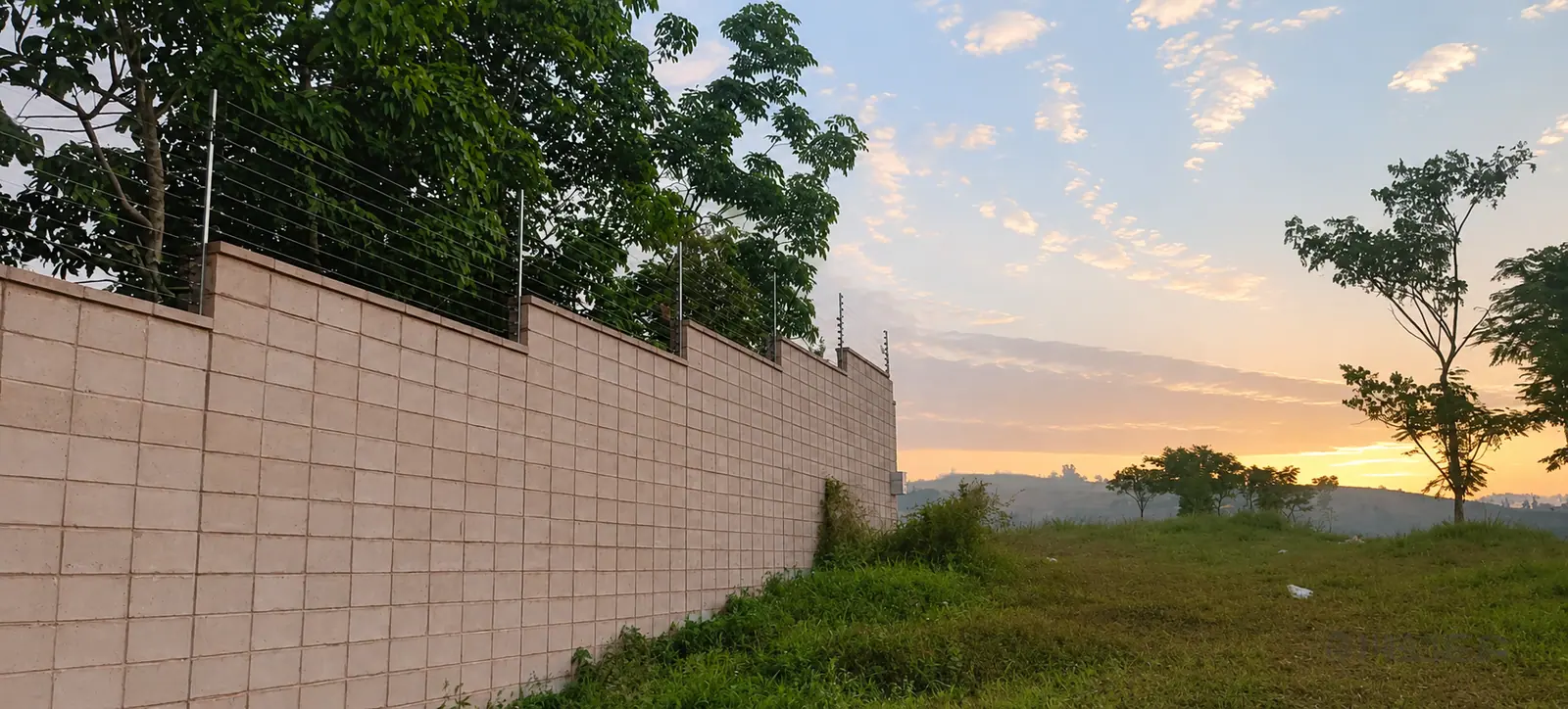 Perimeter electric fence following a boundary wall at sunset
