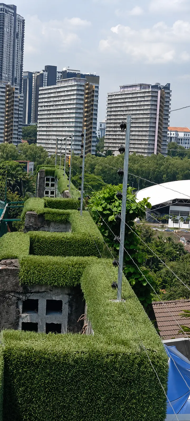 Urban perimeter electric fencing beside landscaped hedges and high-rise buildings