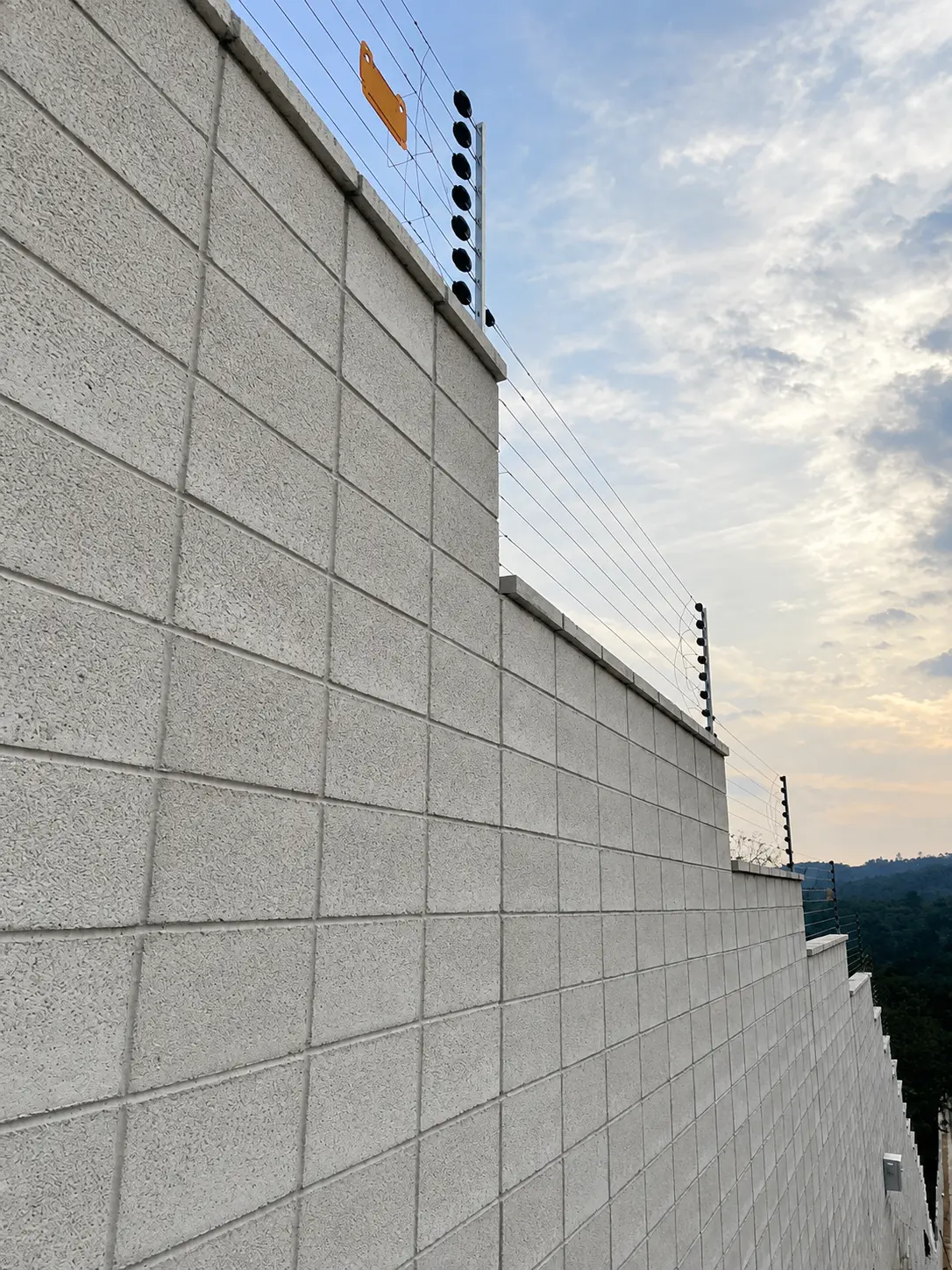 Wall-top electric fencing along a stepped concrete block boundary